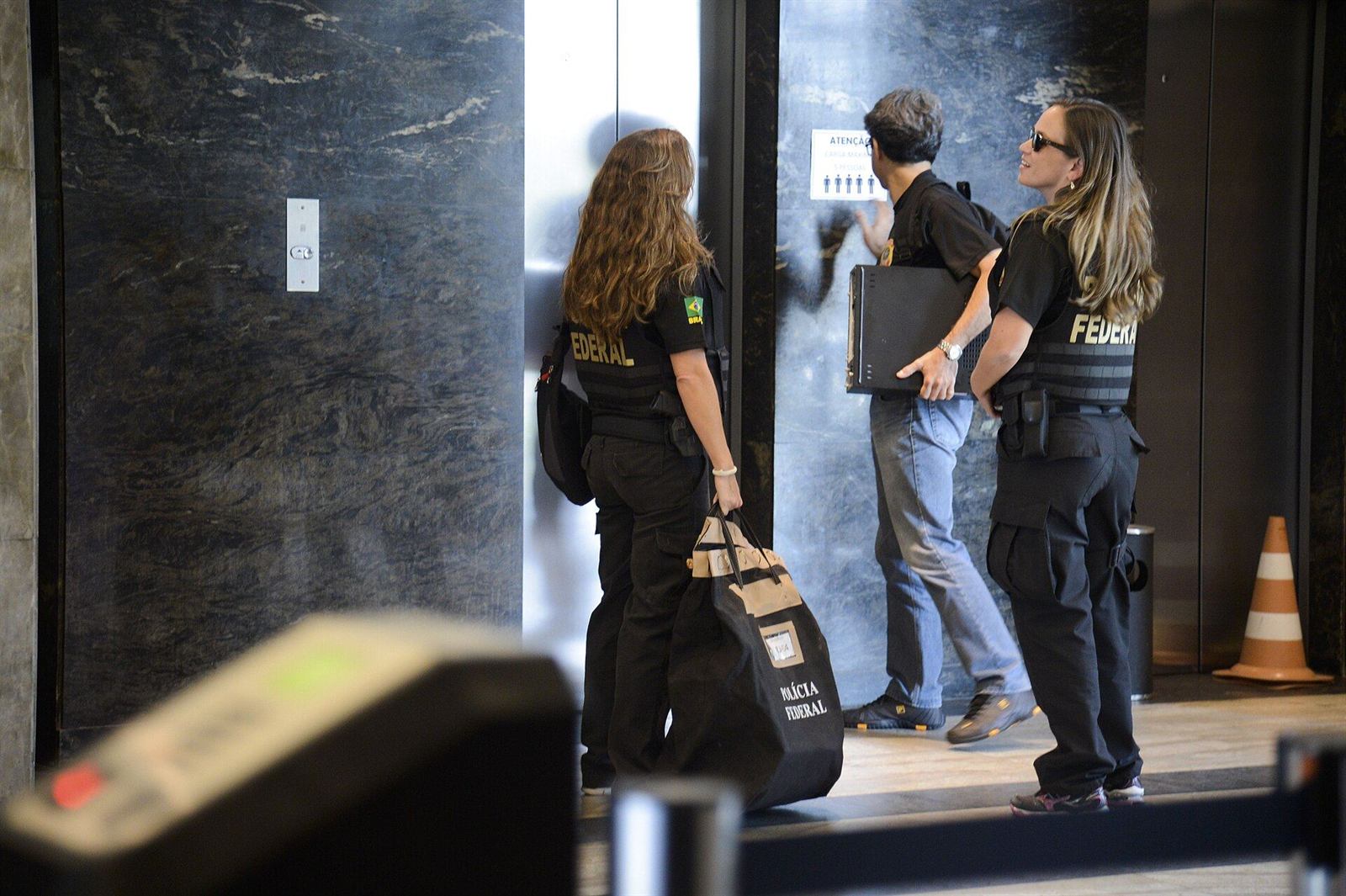 Agentes da Polícia Federal deixam prédio com material apreendido durante operação; imagem ilustrativa.